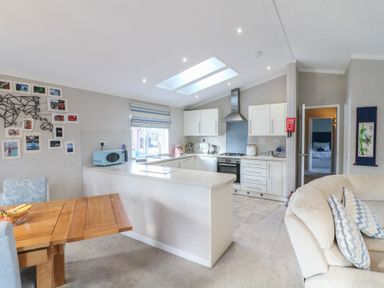 A kitchen with white cabinets and a skylight next to a wooden dining table and a beige sofa at Stones Throw Marston near Barkston