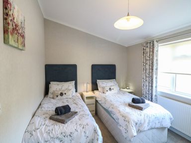 A bedroom with two single beds with bedside tables and a window with curtains at Stones Throw in Marston near Barkston