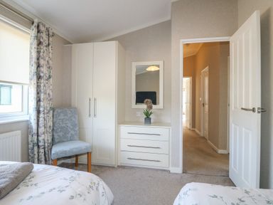 A bedroom with a chair a wardrobe a chest of drawers with a mirror and an open door at Stones Throw in Marston near Barkston