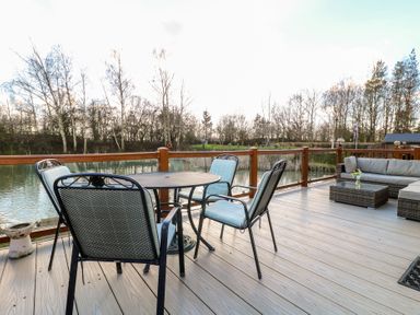 An outdoor deck with a round table and four chairs near a body of water and trees at Stones Throw Marston near Barkston
