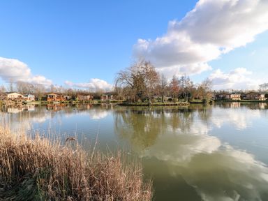 A lake with trees on an island and wooden cabins along the shore at Stones Throw in Marston near Barkston