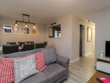 A living room with a gray sofa and pillows and a dining area with a table and chairs at Lewis Lodge in St Ann's Chapel