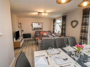 A dining area with table settings and a living room with a sofa and a television at Lewis Lodge in St Anns Chapel