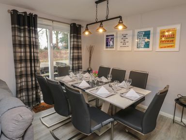 A dining room with a glass table set for eight with black chairs and wall art at Lewis Lodge in St Ann's Chapel