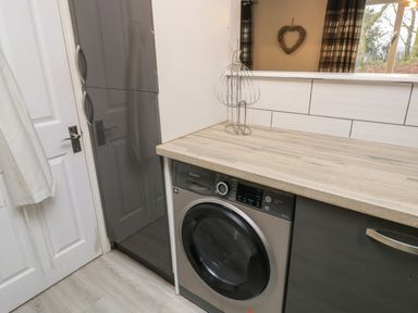 A laundry area with a washing machine below a wooden countertop and a cabinet beside it at Lewis Lodge in St Ann's Chapel