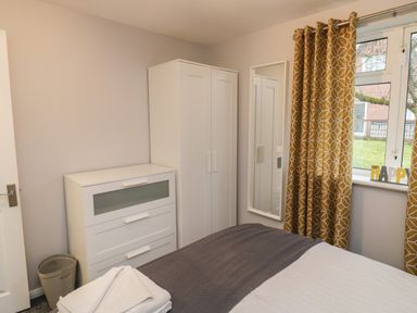 A bedroom with a bed towels a white chest of drawers white wardrobe mirror and window with patterned curtains at Lewis Lodge in St Ann's Chapel