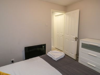 A bedroom with a bed, folded towels on the bed, a white dresser, and an open door at Lewis Lodge in St Ann's Chapel