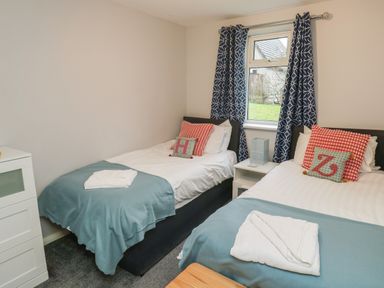 A bedroom with two single beds with folded towels blue blankets and patterned cushions by a window with patterned curtains at Lewis Lodge in St Ann's Chapel