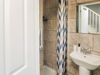 A small bathroom with a shower area with a patterned shower curtain and a sink with soap dispensers at Lewis Lodge in St Ann's Chapel