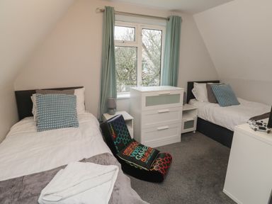 A bedroom with two single beds a window with curtains a white dresser and a gaming chair at Lewis Lodge in St Ann's Chapel