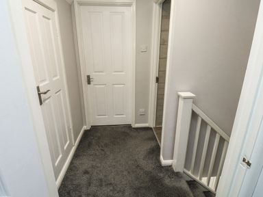 A hallway with three white doors grey carpet and a staircase with white railing at Lewis Lodge in St Ann's Chapel