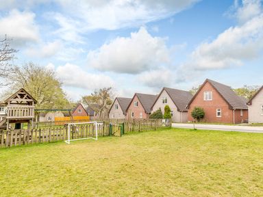 A grassy area with a wooden play structure and fenced playground near houses with pitched roofs at Lewis Lodge in St Ann's Chapel