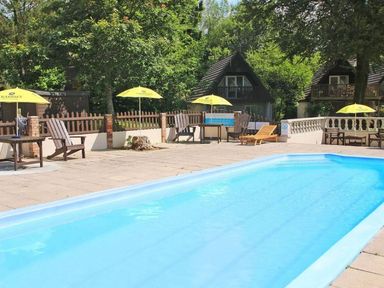 An outdoor swimming pool with lounge chairs wooden Adirondack chairs yellow umbrellas and two small houses in a wooded area at Lewis Lodge in St Ann's Chapel