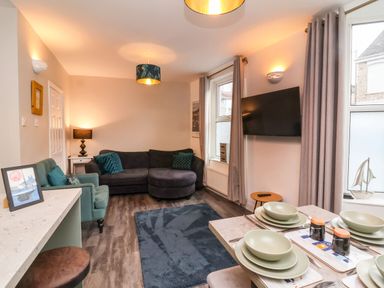 A living room with a sectional sofa an armchair a rug a wall-mounted tv and a dining table set for four at Hollycombe in Ilfracombe