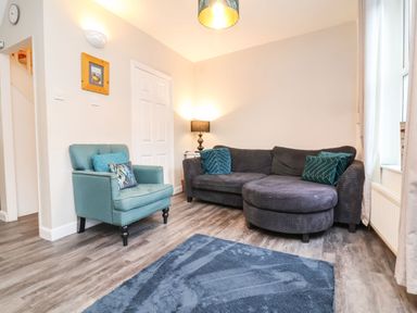 A living room with a gray sectional sofa blue armchair floor lamp blue rug and a window at Hollycombe in Ilfracombe