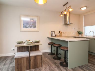 A kitchen with a small dining table set for four and a countertop with three stools at Hollycombe in Ilfracombe