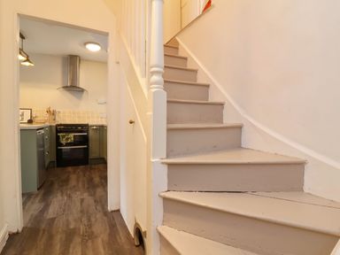 A hallway with stairs leading up and a view into a kitchen with stove and cabinets at Hollycombe in Ilfracombe
