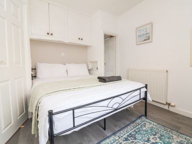 A bedroom with a double bed with white bedding and green blanket under built-in white cabinets at Hollycombe in Ilfracombe