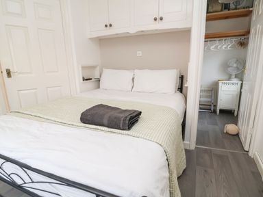 A bedroom with a bed white pillows a folded blanket and towel wooden floor and an open door showing a closet with hangers and a fan at Hollycombe Ilfracombe
