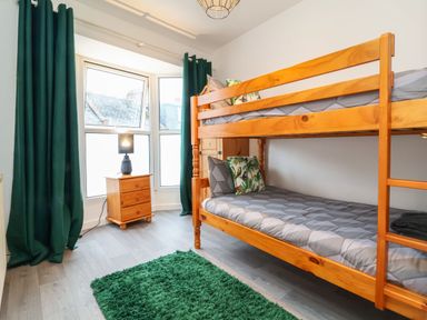 A bedroom with a wooden bunk bed a bedside table with a lamp green curtains and a green rug at Hollycombe in Ilfracombe