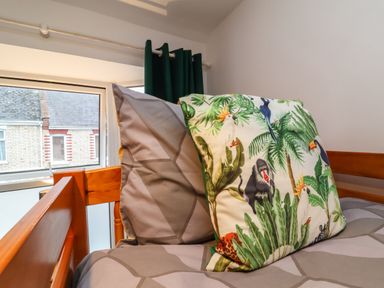 A bed with patterned pillows and a window with green curtains in a bedroom at Hollycombe in Ilfracombe
