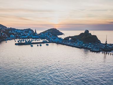 A harbor with boats docked near a town at sunset with hills and a small building on a hill overlooking the water at Hollycombe Ilfracombe