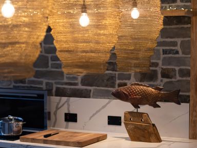 A kitchen countertop with a wooden cutting board and knife a metal pot and a fish sculpture on a wooden base at Oystercatcher in Mevagissey