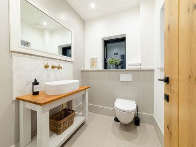 A bathroom with a wooden door a wall-mounted toilet a sink with a wooden countertop and a large mirror at Oystercatcher in Mevagissey