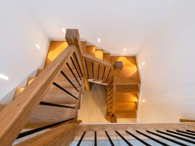 A wooden staircase with black metal balusters and white walls at Oystercatcher in Mevagissey