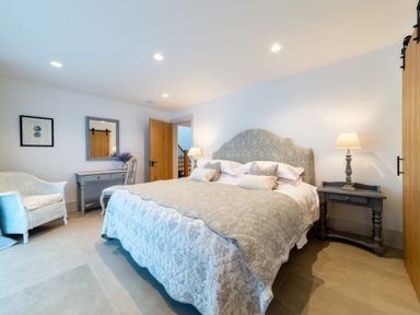 A bedroom with a large bed bedside tables lamps a desk chair wicker armchair and wooden doors at Oystercatcher in Mevagissey