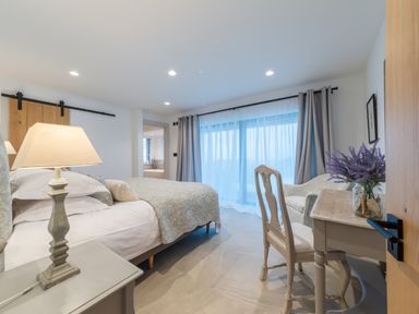 A bedroom with a bed lamps a desk and chair next to a window with curtains at Oystercatcher in Mevagissey