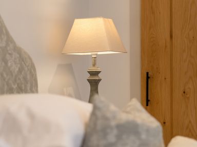A table lamp with a beige shade near a wooden door in a bedroom at Oystercatcher in Mevagissey