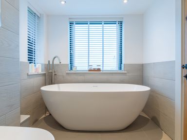 A bathroom with a freestanding bathtub and windows with blinds at Oystercatcher in Mevagissey