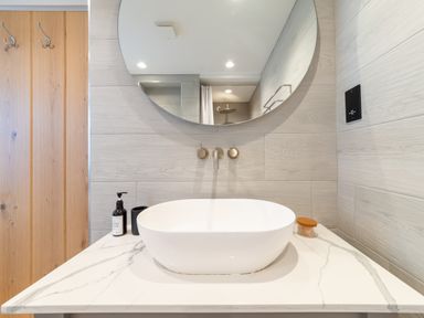 A bathroom sink with a round mirror above and wooden hooks on the wall at Oystercatcher in Mevagissey