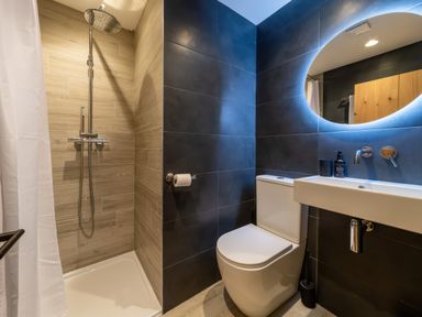 A bathroom with a shower area a toilet a sink and an oval mirror at Oystercatcher Mevagissey