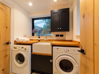 A laundry room with a washing machine dryer sink wooden countertops and black cabinets at Oystercatcher Mevagissey