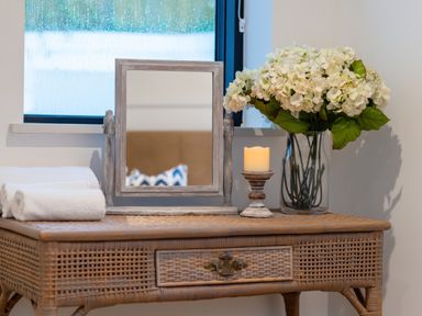 A wicker table with a mirror towel candle and vase of flowers at Oystercatcher in Mevagissey