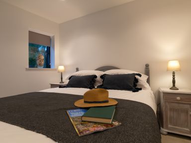A bedroom with a double bed lamps on bedside tables and a window with a vase of shells at Oystercatcher Mevagissey