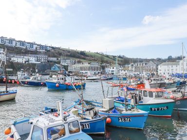 Fishing boats docked in a harbor with buildings and hills in the background at Oystercatcher Mevagissey
