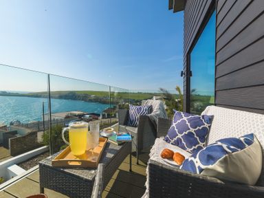 A balcony with wicker chairs cups books and a pitcher of lemonade overlooking the sea at Oystercatcher in Mevagissey