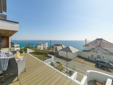 A balcony with wicker chairs and glass railing overlooking the sea and neighboring houses at Oystercatcher in Mevagissey