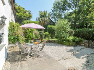 An outdoor patio with a round table and four chairs under a pink umbrella in a garden at 2 Rose Cottage in St Agnes
