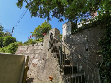 An outdoor stone staircase with a metal railing leading to a garden area surrounded by greenery at 2 Rose Cottage in St Agnes