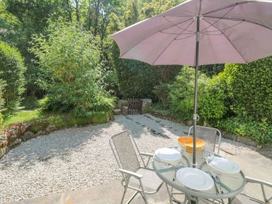 A garden patio with a glass table set for three under a large umbrella at 2 Rose Cottage in St Agnes
