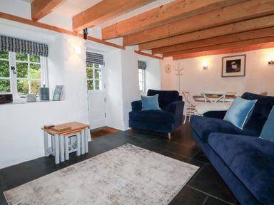 A living room with blue armchairs and sofa a wooden ceiling and a dining table at 2 Rose Cottage in St Agnes
