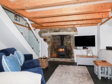 A living room with a blue sofa a stone fireplace with wood burner and a tv on a stand at 2 Rose Cottage in St Agnes