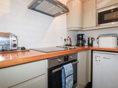 A kitchen with a wooden countertop and white cabinets including a toaster kettle coffee maker and microwave at 2 Rose Cottage in St Agnes