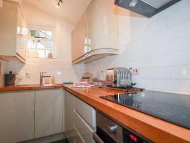 A small kitchen with wooden countertops a stainless steel toaster an electric stovetop and a window above the sink at 2 Rose Cottage in St Agnes