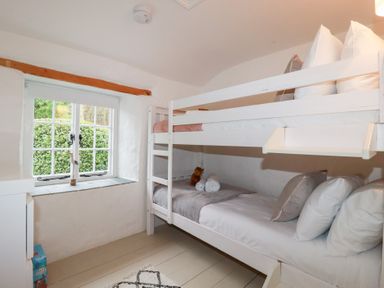 A bedroom with white bunk beds and a window with wooden beam at 2 Rose Cottage in St Agnes