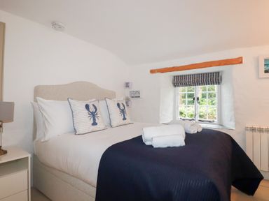 A bedroom with a bed with lobster pillows and folded towels by a window at 2 Rose Cottage in St Agnes